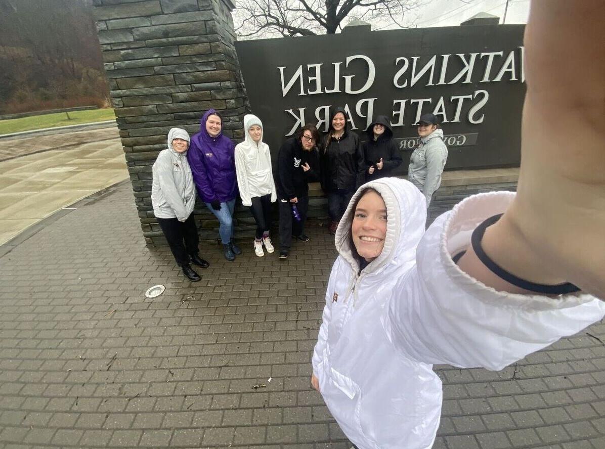 Hiking Club members pose for a group selfie in front of the Watkins Glen State Park sign